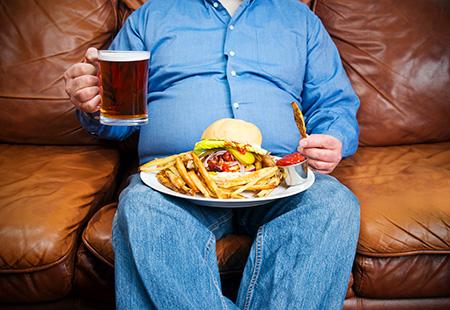 Overweight man on sofa with junk food