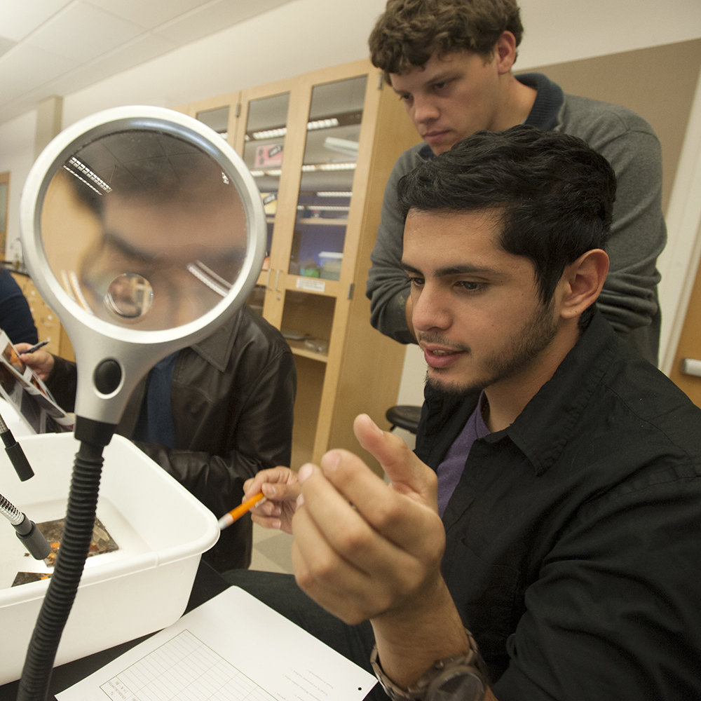 Two male students sitting beside a magnifying glass. 