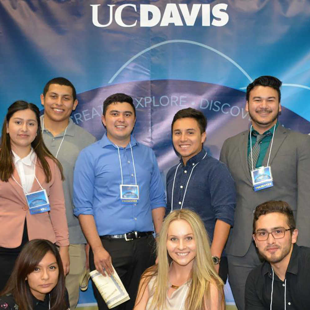 Group shot of diverse students standing in front of a UC Davis banner