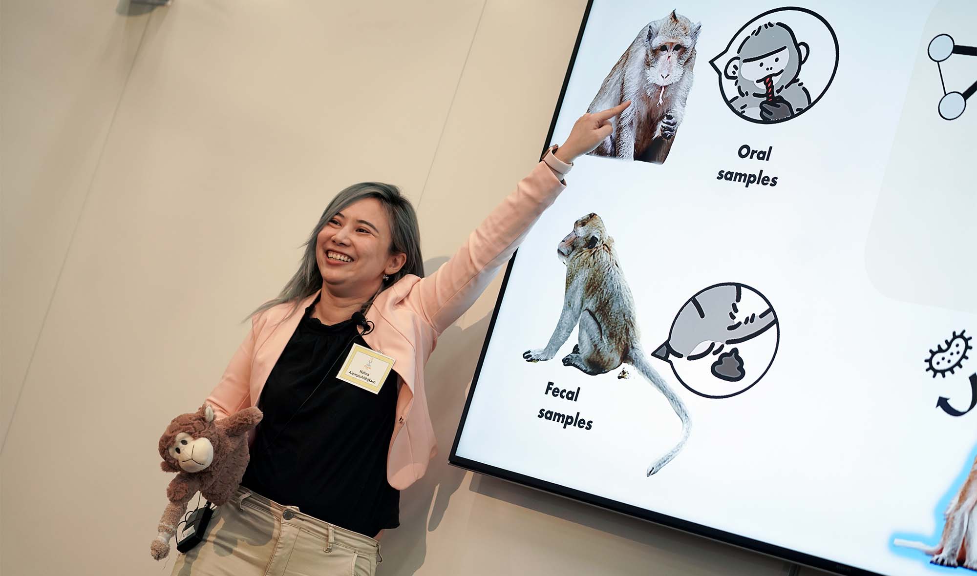 Female presenter standing beside presentation screen and pointing to an image of a monkey