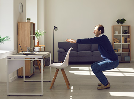 Man in office setting doing a squat exercise. 