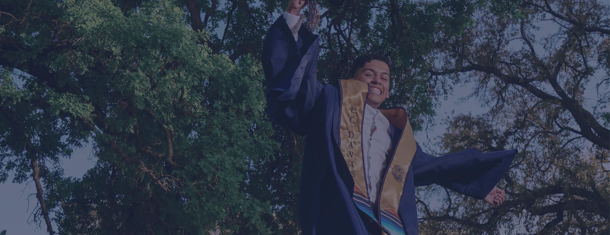 Male student in graduation robes jumping into the air in celebration