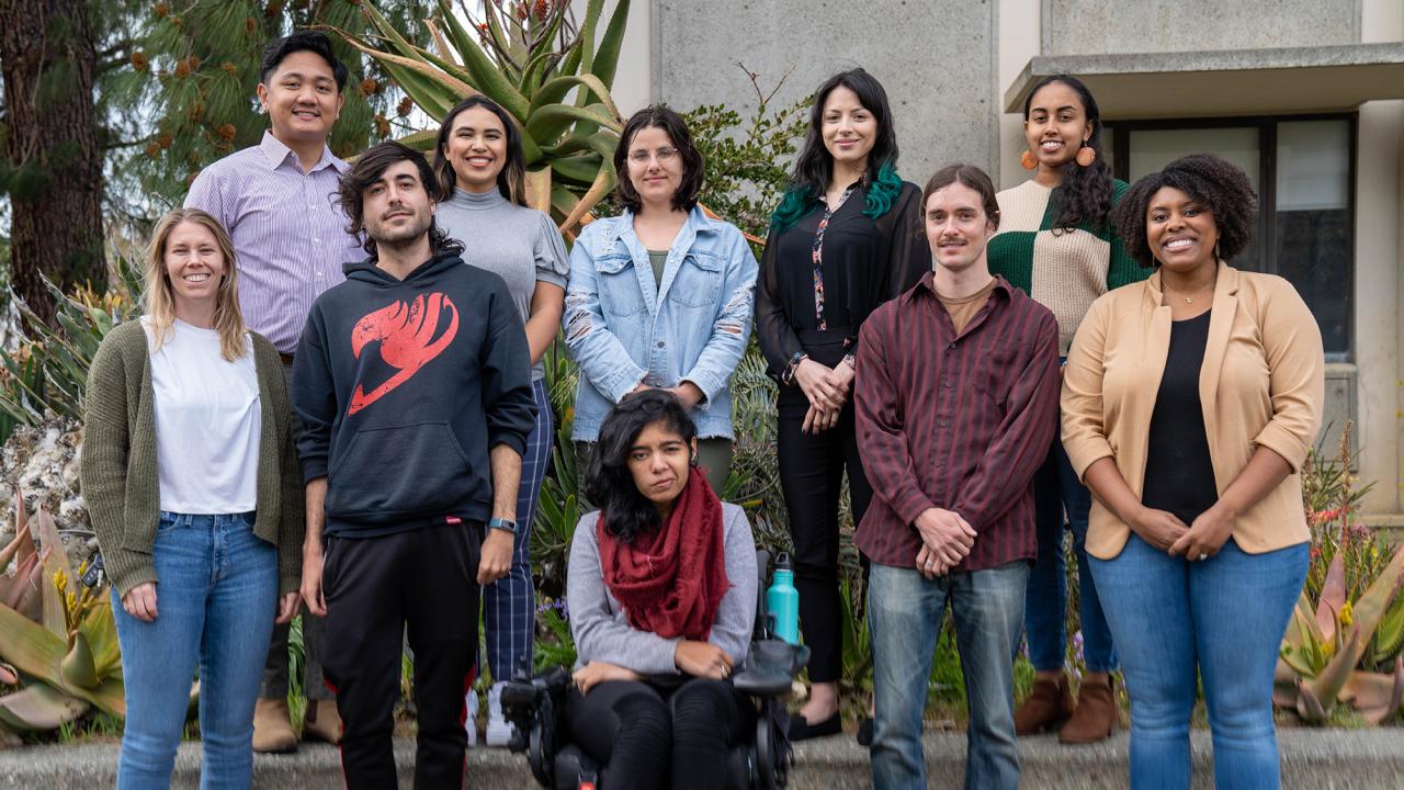 A group shot of male and female graduate students standing outside with succulents behind them.