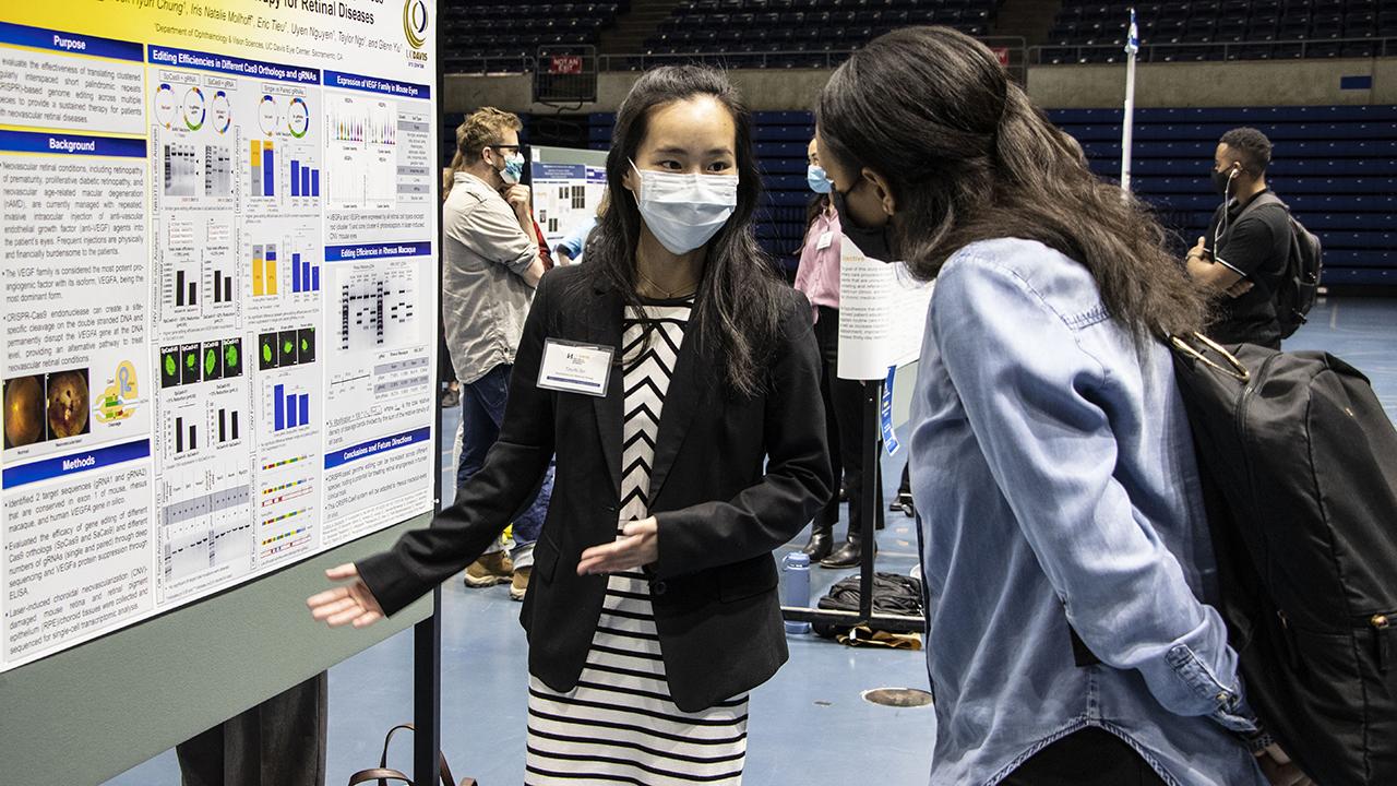 Two female students with masks looking at research poster