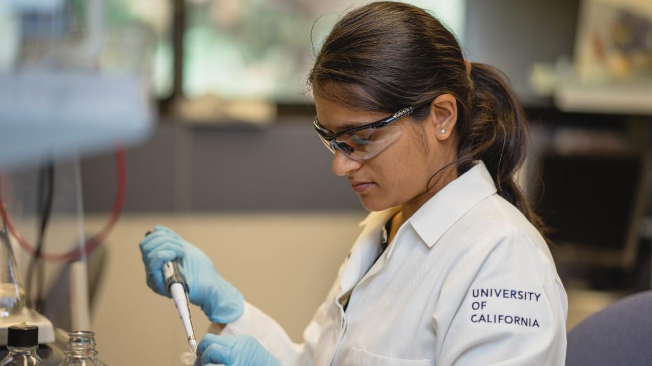 Female researcher in lab coat with goggles using a pipette