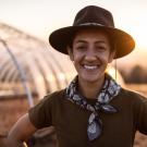 Marina LaForgia in hat standing in a field at sunset