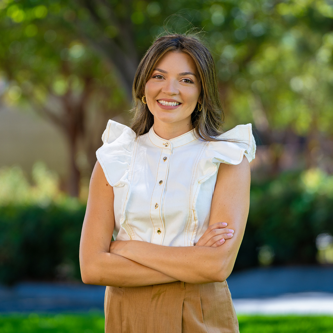 Outdoor portrait of smiling young woman with arms crossed, white ruffled blouse
