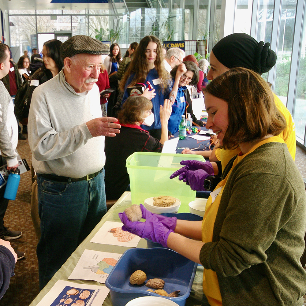 A man at a NeuroFest display booth talking to the two women behind the table. 
