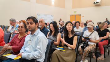 Audience seated and attentive during a formal ceremony. Program pamphlets in hand, expressions vary between interest and concentration.