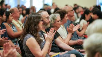 Audience claps during awards ceremony. Individuals show appreciation for speaker or recipient, programs visible on laps and in hands.
