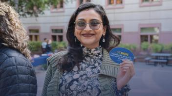 Person with long dark hair holding a UC Davis sticker