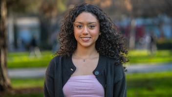 A person with long curly hair in a white shirt standing outside