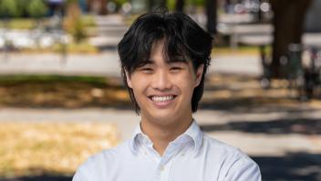 A person in a white button down shirt standing outside in front of trees