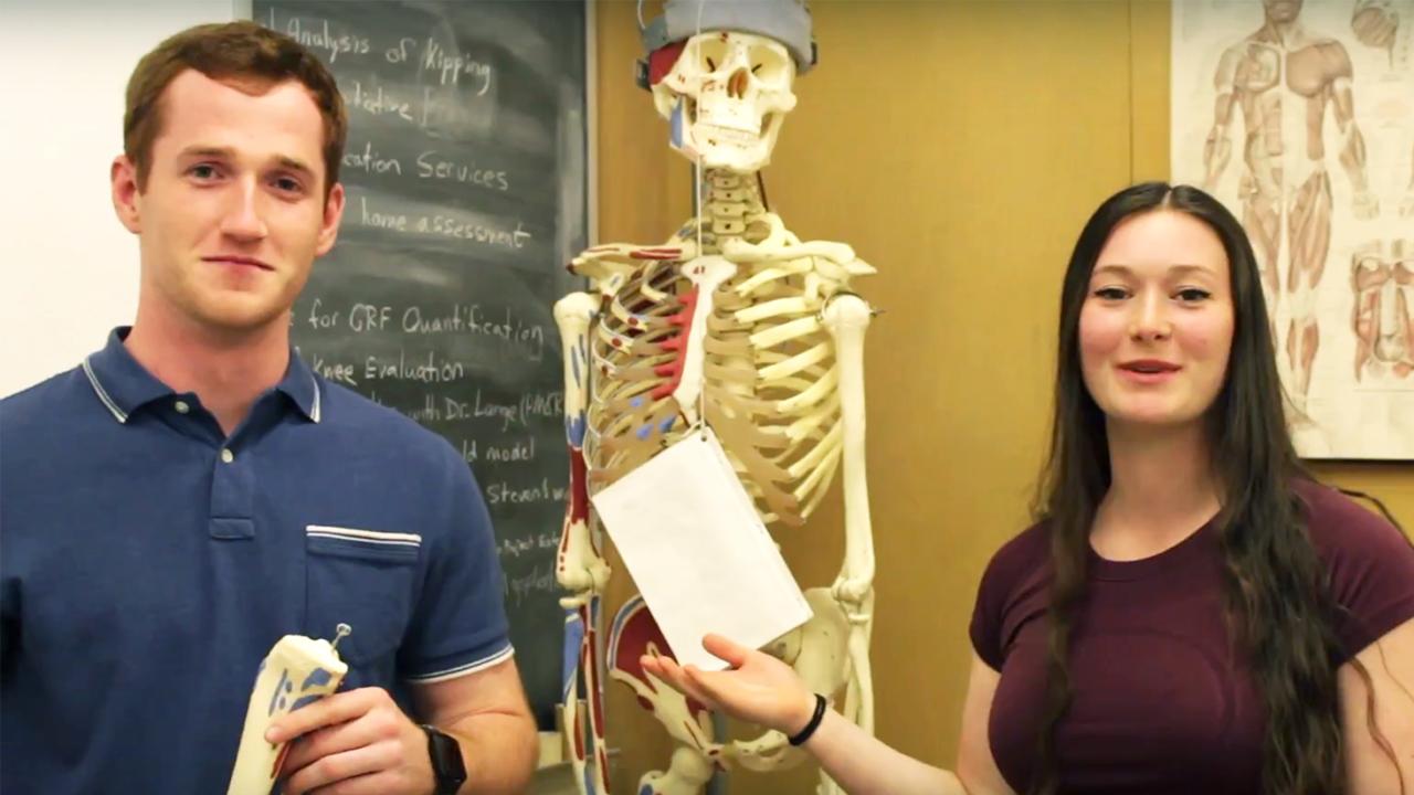 Tanner Van Es and Jennifer Addleman stand near a skeleton in the Human Performance Lab