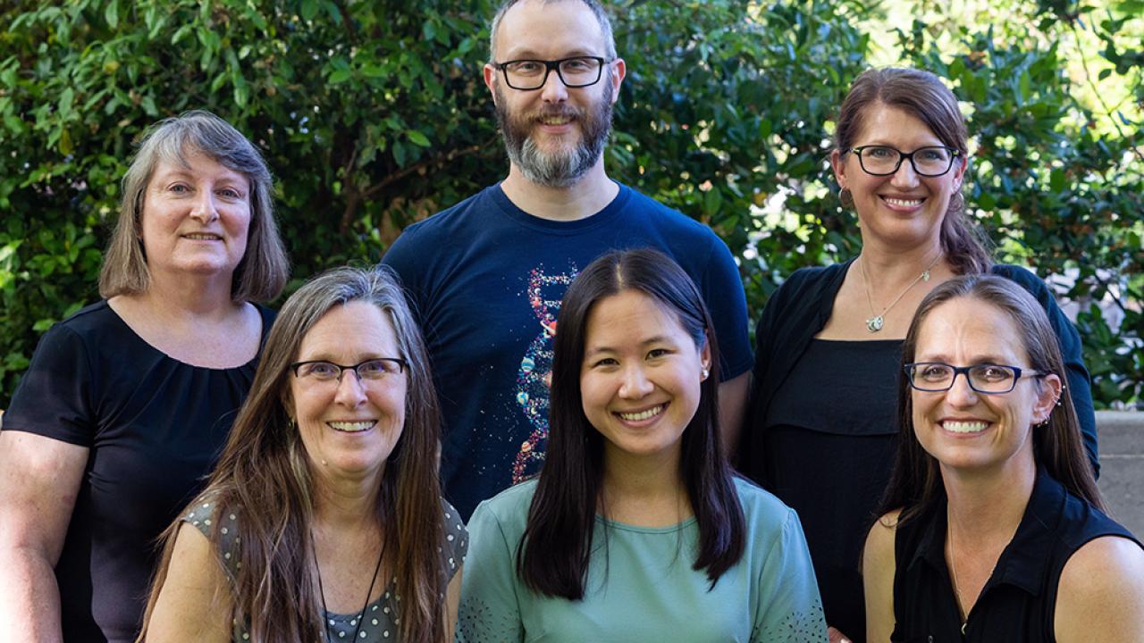 Group shot of people standing outside in front of a tree. 