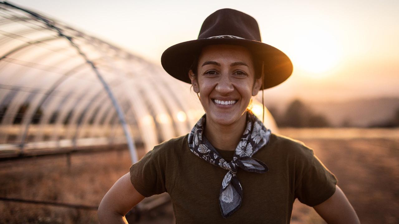 Marina LaForgia in hat standing in a field at sunset