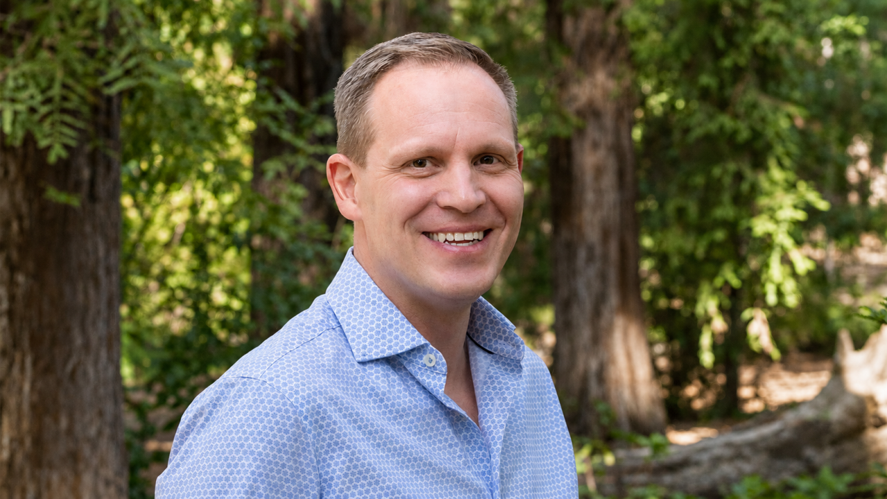 Smiling man in blue shirt, outdoor portrait with trees and dappled sunlight