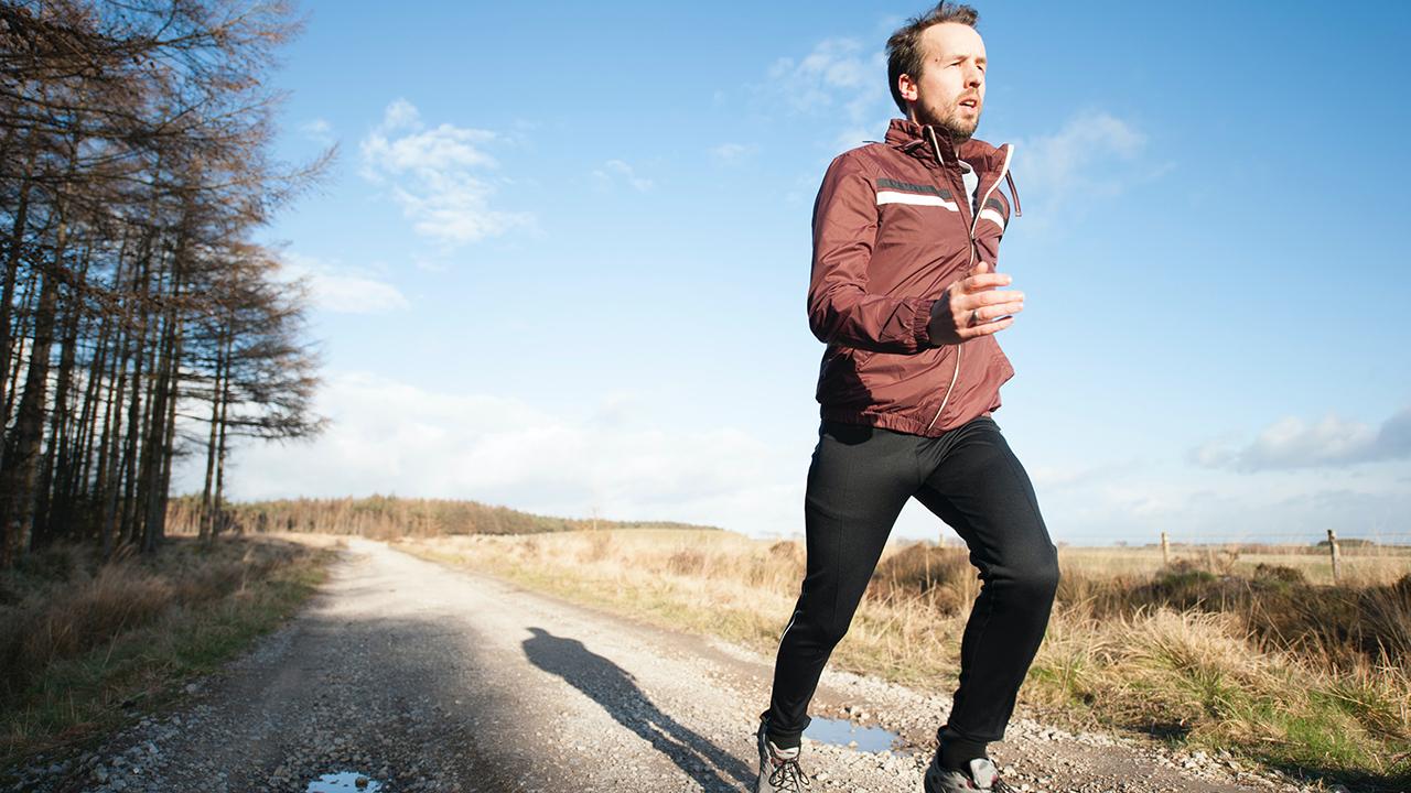 Man running outdoors along path beside trees. 