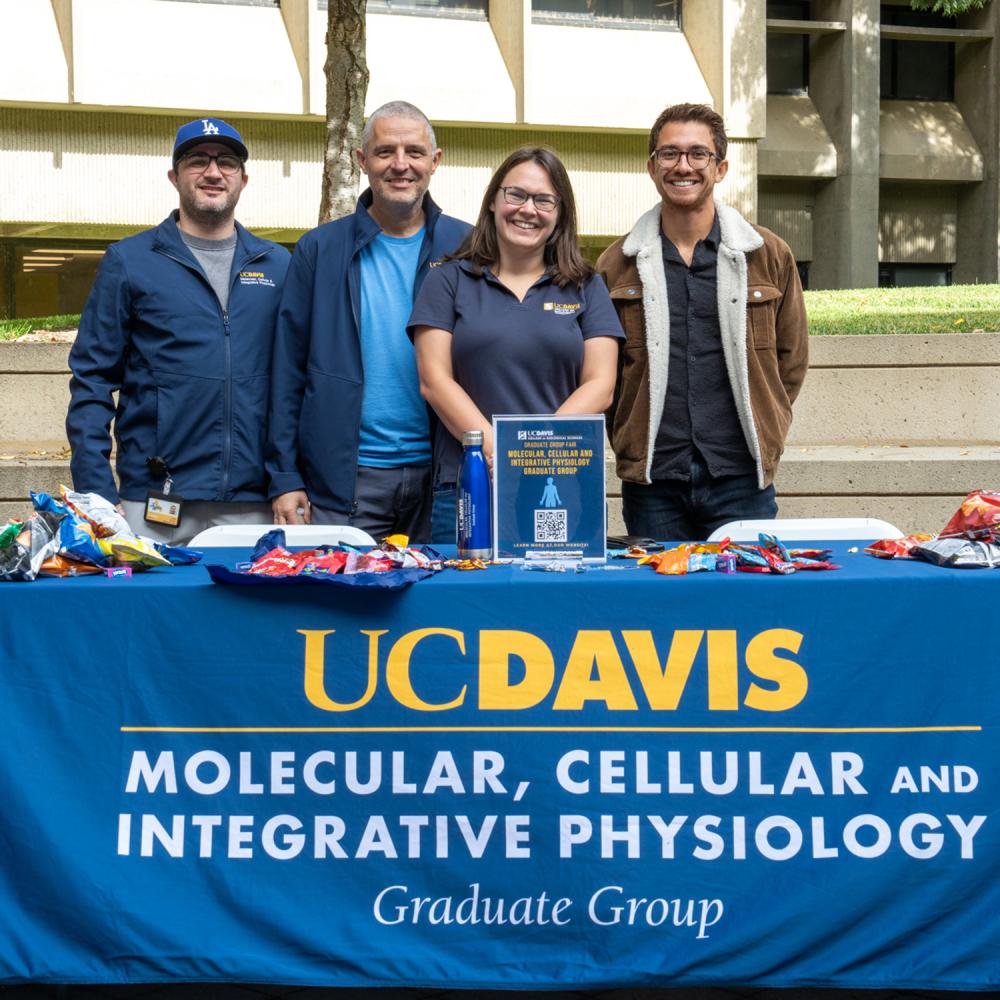 Four students and faculty members smile at a UC Davis Molecular, Cellular and Integrative Physiology table during an advising event.