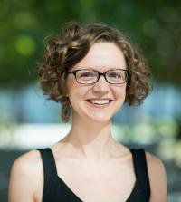 A person with curly hair in a blakc tank top standing outside