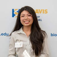 Smiling woman with glasses and long dark hair, holding a glass award in front of UC Davis logo