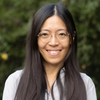Smiling woman with long dark hair and glasses in an outdoor headshot