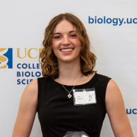Smiling young woman in black dress with name tag in front of university banner, photograph