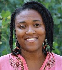 A person with braided hair in a pink shirt standing outside