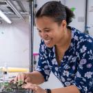 Smiling woman in floral blouse assembling electronics on a lab workbench