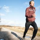 Man running outdoors along path beside trees. 