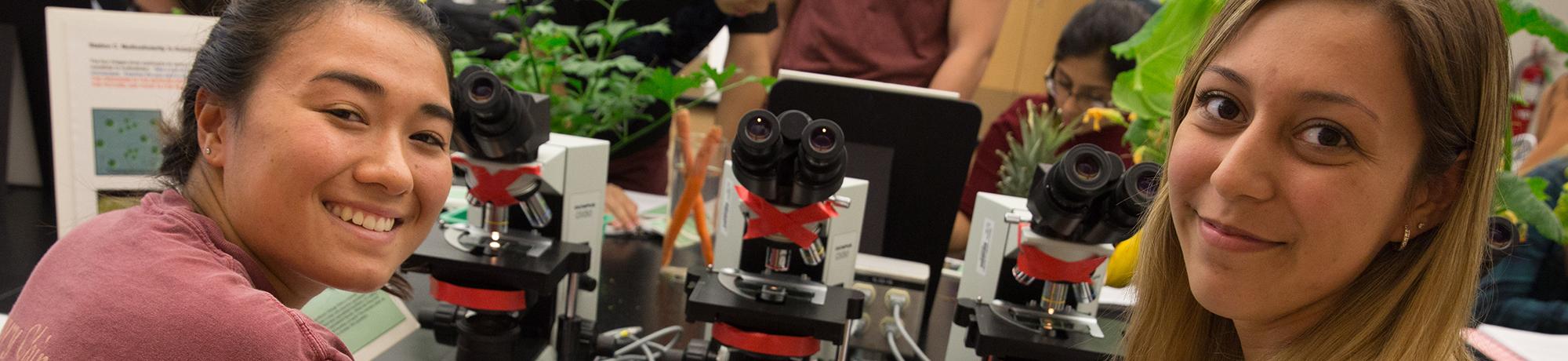Two female students in classroom setting with microscope